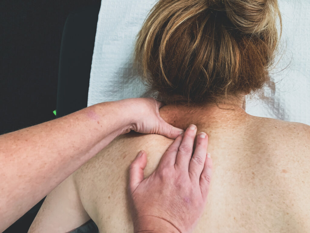 This image shows a client laying face down on a treatment bed. You can only see from the upper back to their head. They are receiving a Remedial Massage on their neck.