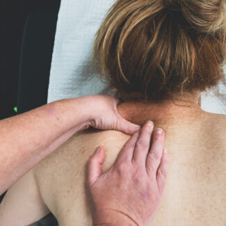 This image shows a client laying face down on a treatment bed. You can only see from the upper back to their head. They are receiving a Remedial Massage on their neck.
