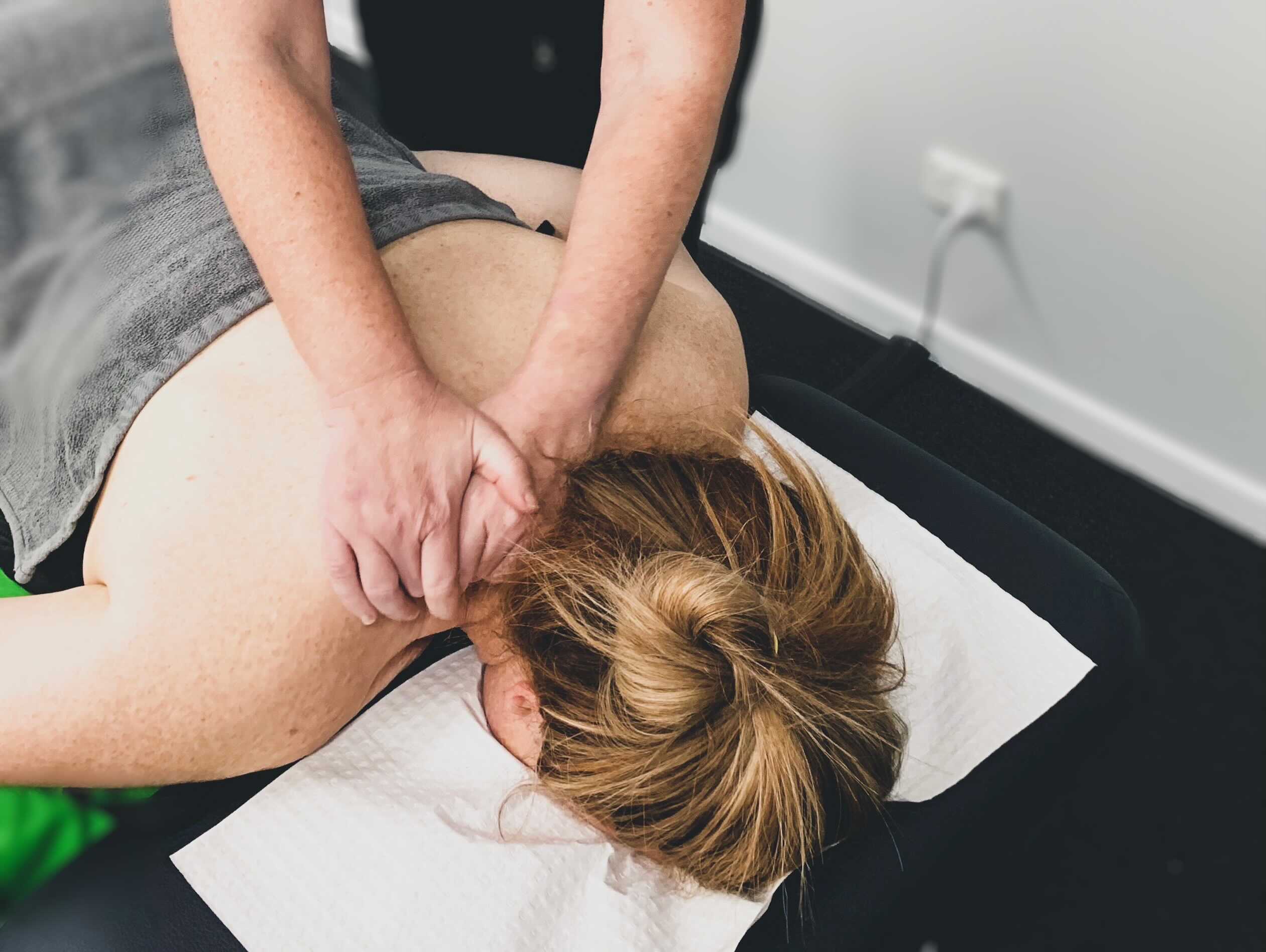 This image shows a client receiving a neck massage. They are laying face down on the treatment bed and our Remedial Massage Therapist, Heather, is pressing into a pressure point on the client's neck.